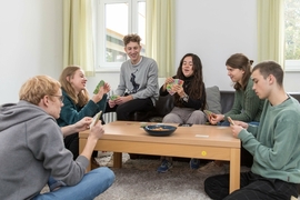 Gruppe junger Menschen spielt Karten in einer Wohngruppe.